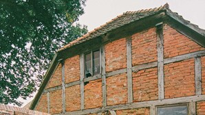 Zona d'estar a l'exterior rústica amb paret de maó, bigues de fusta i una ombrellida blanca.
