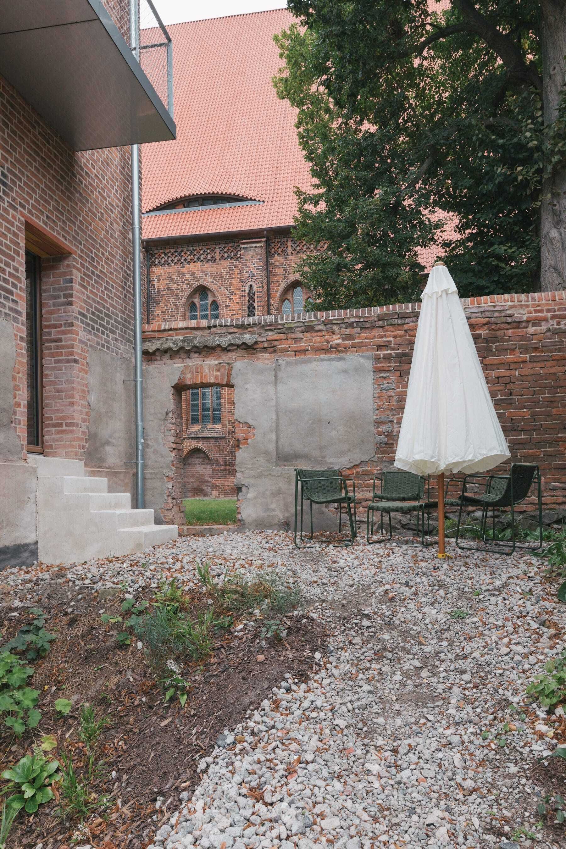 Un patio con un edificio de ladrillo, una sombrilla blanca y dos sillas.