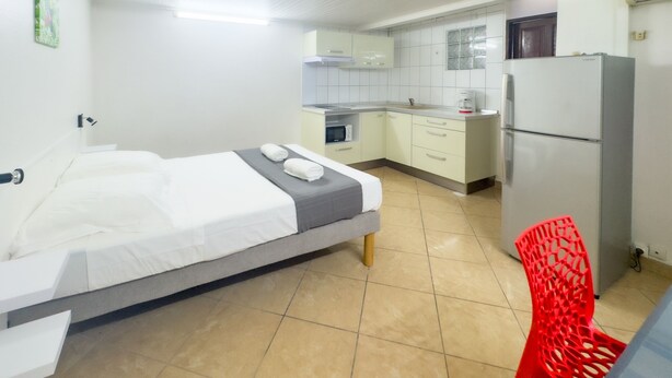 A bedroom with a bed, a red chair, and a kitchenette with a refrigerator and microwave.