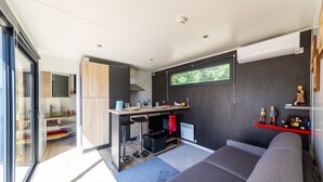 Cozinha moderna com área de bar, sofá cinza e prateleira vermelha com objetos decorativos.