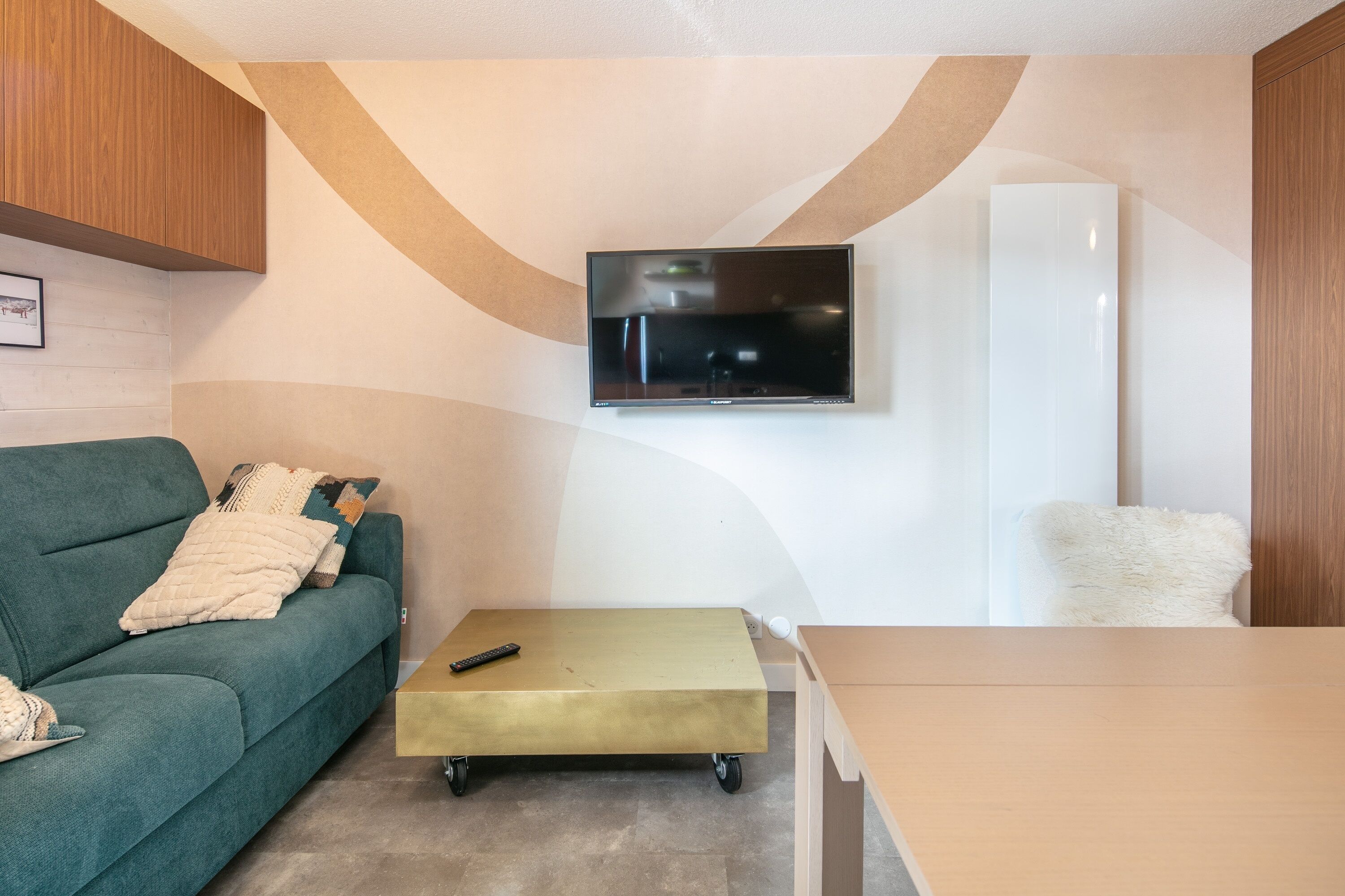 Un salon moderne avec un canapé vert, une petite table et un téléviseur fixé au mur.