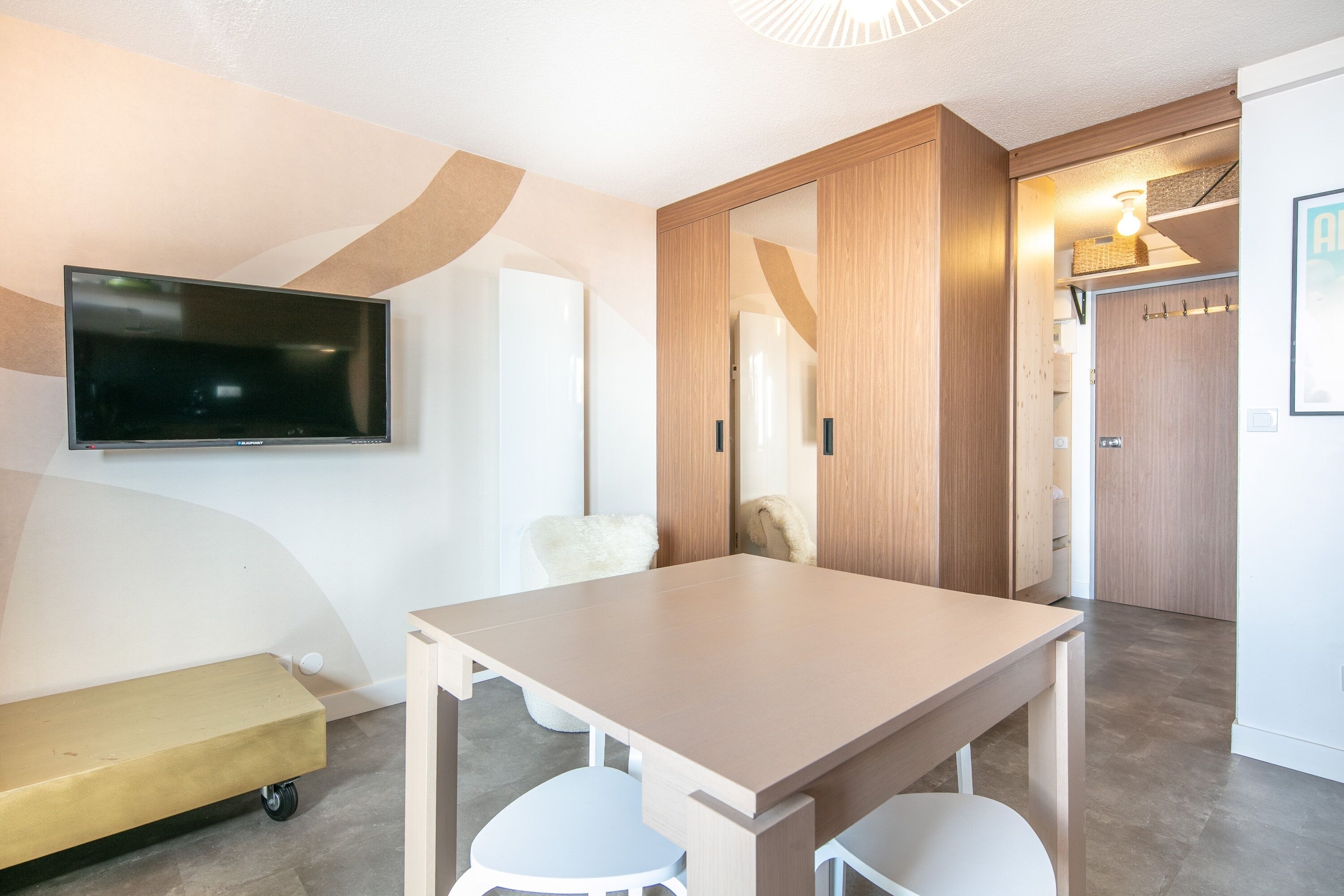 Habitació d'hotel moderna amb televisió de pantalla plana penjada a la paret, armari de fusta, zona de seients petita amb una banca i taula amb dues cadires.