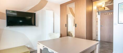 Habitació d'hotel moderna amb televisió de pantalla plana penjada a la paret, armari de fusta, zona de seients petita amb una banca i taula amb dues cadires.