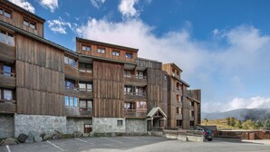Un edificio de madera de varios pisos con balcones, base de piedra y un área de estacionamiento.
