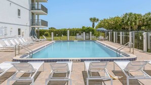 A rectangular swimming pool with a tiled edge, surrounded by white lounge chairs and a fence. - Aloha Awaits - 2B/2B Ground Floor Condo (Cape Canaveral)