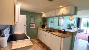 A compact kitchen with white cabinets, a granite countertop, and a small island. - Aloha Awaits - 2B/2B Ground Floor Condo (Cape Canaveral)