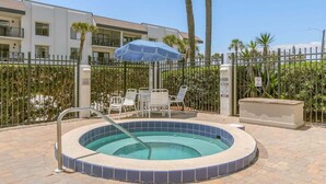 A swimming pool with a tiled edge, surrounded by a fence, and a lounge area with chairs and an umbrella. - Aloha Awaits - 2B/2B Ground Floor Condo (Cape Canaveral)