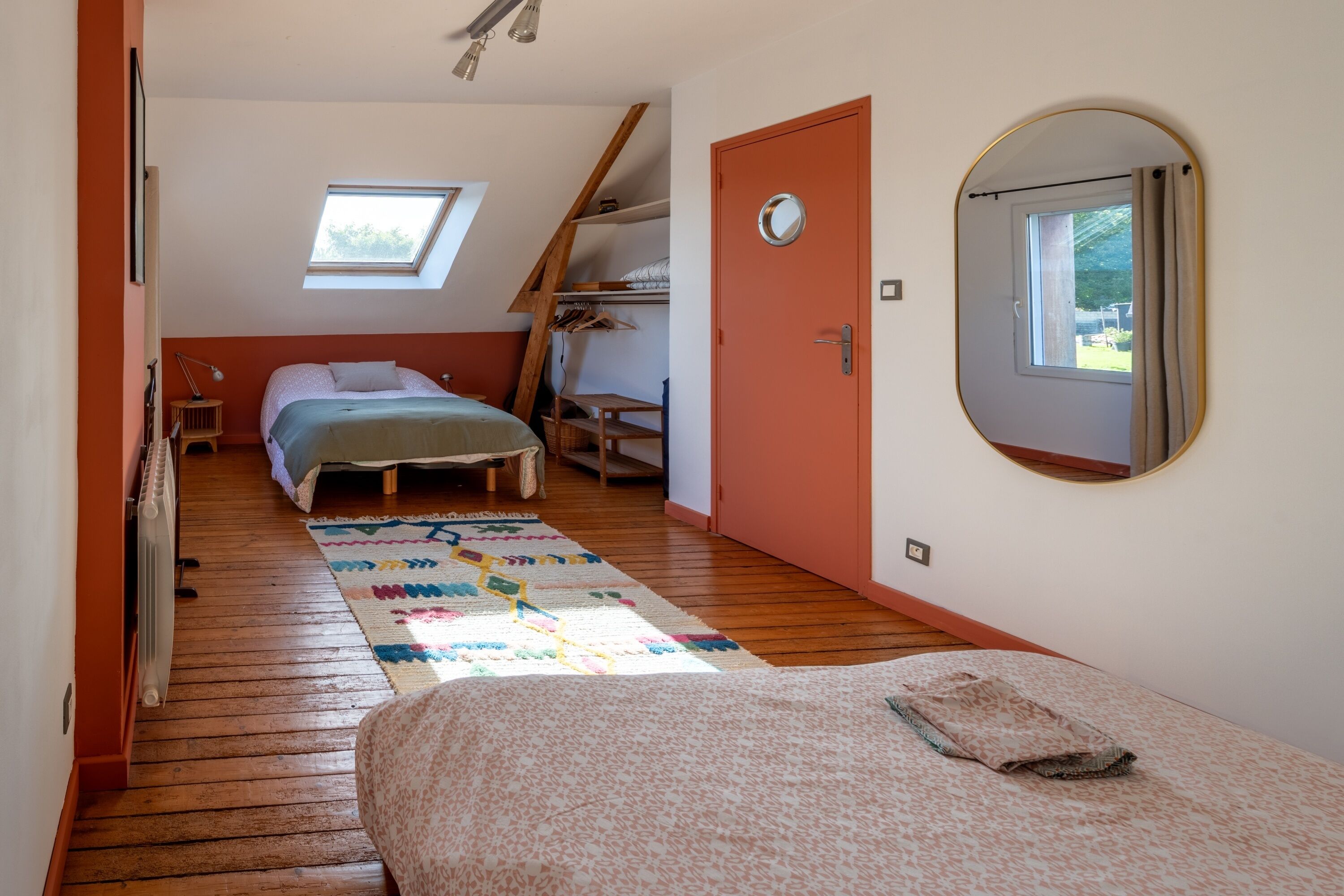 Un dormitorio con techo inclinado, tragaluz, cama con cubrecama estampado, una mesita pequeña y un armario.
