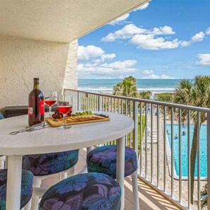 Ein Balkon mit Tisch für zwei Personen, einer Flasche Rotwein und einem Weinglas. Blick auf einen Swimmingpool und den Ozean.