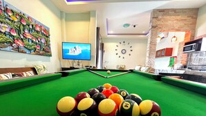 Ein Billardtisch mit Kugeln, ein Fernseher und eine Uhr an der Wand.