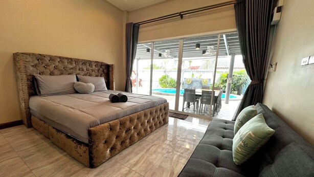 Ein Schlafzimmer mit einem großen Bett, einer Couch und einer Glasschiebetür, die zu einem Außenbereich mit Pool und Esstisch führt.