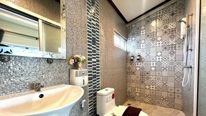 Ein Badezimmer mit einem großen, weißen Waschbecken, einer Toilette und einem Duschbereich mit gemusterten Fliesen.