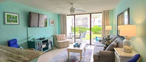Una sala de estar con sofá, sillones, una mesa de centro, televisor y un balcón con mobiliario exterior.