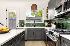 A modern kitchen with grey cabinets, a stainless steel stove, and a window with a view of the outside. - Sleeps 12, Pool, Games, Fun, Mins from Downtown (Austin)