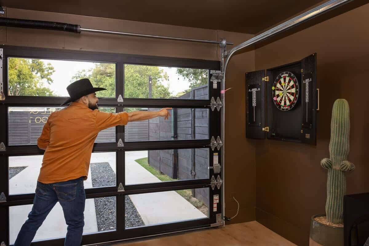 Um homem com camisa laranja e chapéu preto abrindo uma porta de garagem.