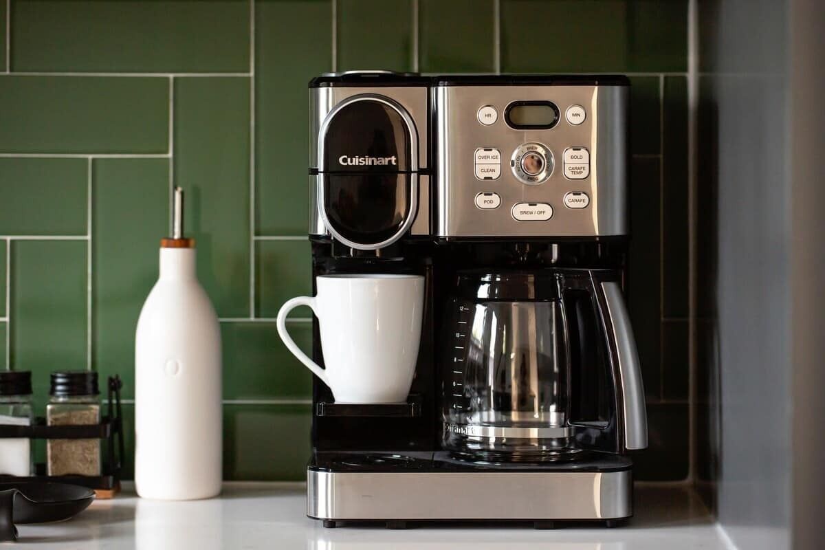 A Cuisinart coffee maker with a white cup holder, a white water bottle, and a coffee pot on a kitchen counter.