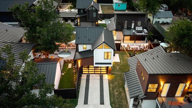 A modern residential area with a central house featuring a prominent garage, a driveway, and a well-maintained lawn.