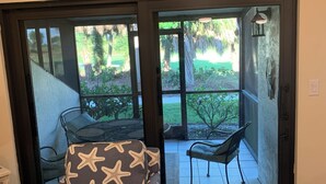 A room with a sliding glass door leading to an outdoor patio area. Inside, there is a sofa with a starfish pattern, a chair, and a small table. - ATTENTION GOLF LOVERS / HAMMOCK BAY GOLF COURSE, NAPLES FL./ CLOSE TO BEACHES (Naples)