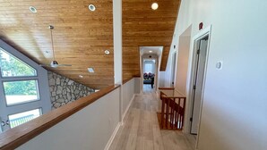 Techo de madera con iluminación empotrada, pared de piedra y vista a un dormitorio con cama y ventana.
