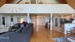 Un loft espacioso con techo alto, pisos de madera, un sofá seccional gris grande y una zona de cocina.