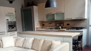Une cuisine moderne dotée d’un four encastré, d’un coin repas avec un canapé beige et d’un luminaire suspendu noir.