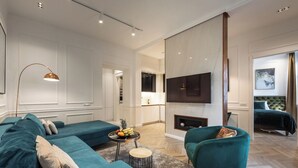 Un salon moderne avec des canapés de couleur turquoise, une table basse ronde ornée de fruits, une cheminée et un téléviseur fixé au mur.