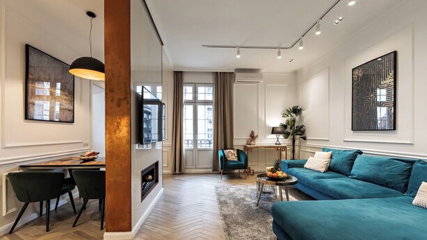 Un salon moderne avec un parquet en chevrons, un canapé de couleur turquoise, un coin repas avec une table et des chaises en bois, et des œuvres d’art accrochées aux murs.