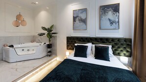Une chambre moderne avec un grand lit, une salle de bain séparée dotée d’un jacuzzi et deux œuvres d’art encadrées accrochées au mur.