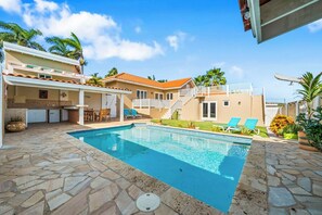 A two-story house with a swimming pool, outdoor seating, and a staircase leading to a balcony.