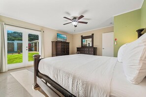 A bedroom with a large bed, a ceiling fan, a dresser, a mirror, and a sliding glass door leading to a balcony.