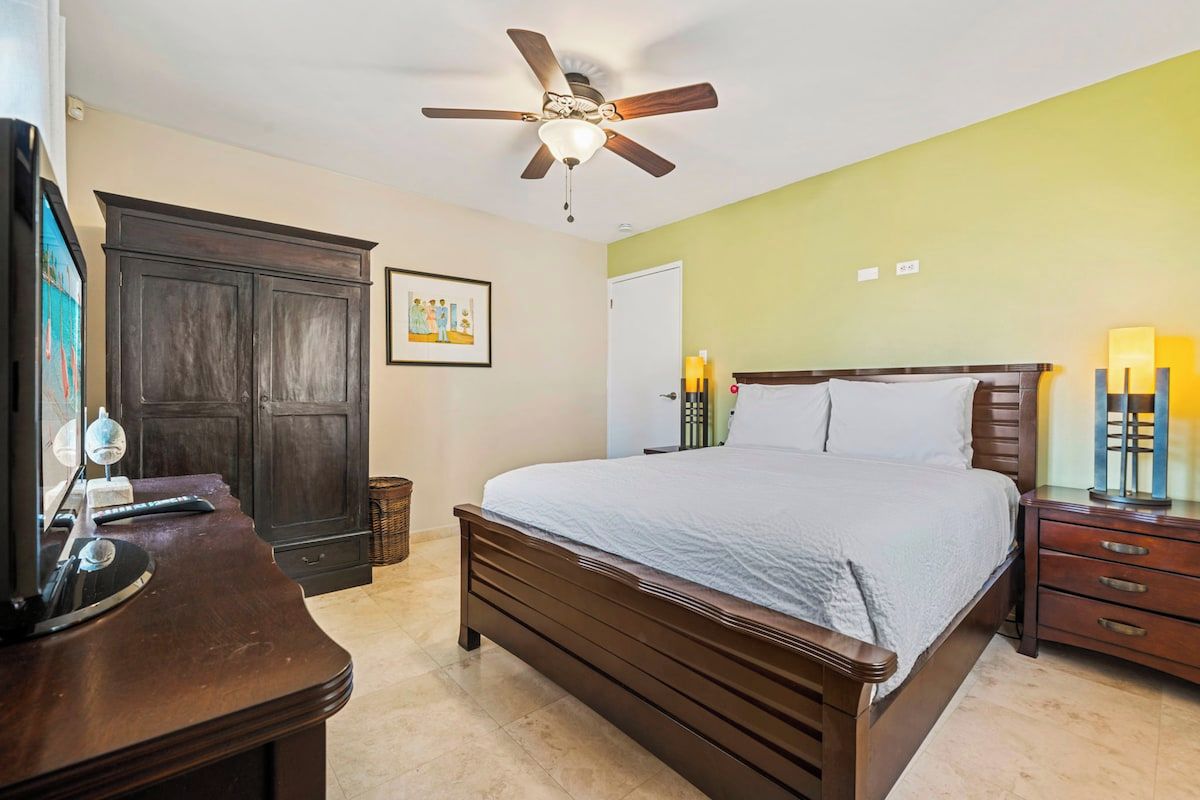 A bedroom with a bed, a desk, a wardrobe, a ceiling fan, and a nightstand with lamps.