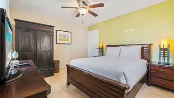 A bedroom with a bed, a desk, a wardrobe, a ceiling fan, and a nightstand with lamps.