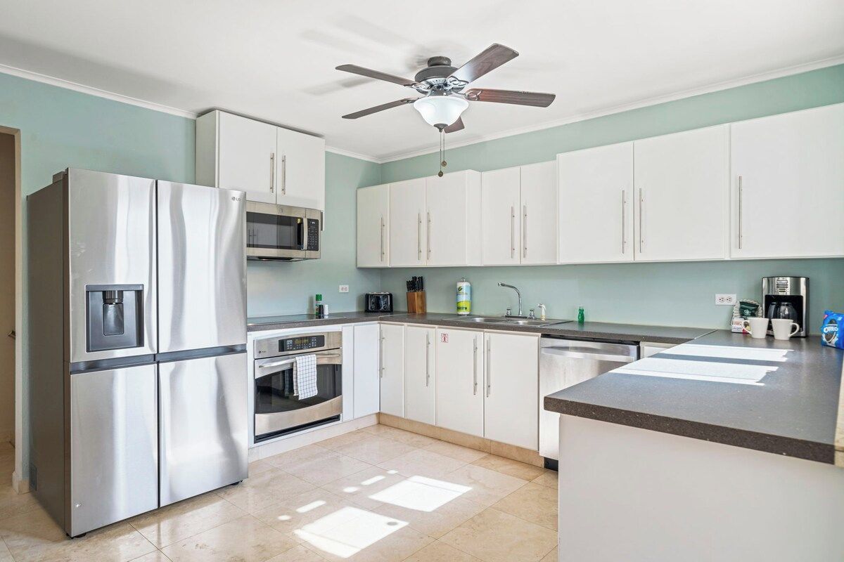 A kitchen with white cabinets, a stainless steel refrigerator, a microwave, and a ceiling fan.