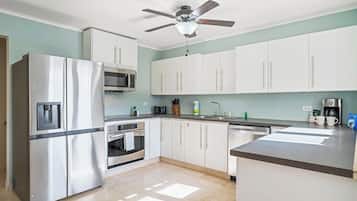A kitchen with white cabinets, a stainless steel refrigerator, a microwave, and a ceiling fan.
