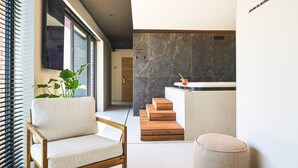 A modern interior with a wooden chair, a small round ottoman, a staircase, and a bar area with a drink. - Clos du Riez - Suites & SPA (La Gorgue)