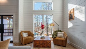 Un salon moderne avec deux canapés marron à revêtement en tissu, une table basse en bois et une grande fenêtre donnant sur des arbres.