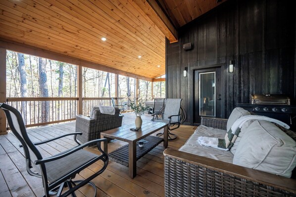 A covered outdoor area with wooden flooring, wicker furniture, and a grill.