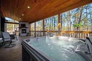 Una vasca idromassaggio su un pontile di legno con un caminetto e posti a sedere all'aperto.