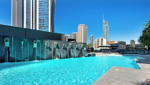 A swimming pool with clear blue water, surrounded by high-rise buildings and a modern architectural structure in the background. - Circle on Cavill - Level 19 - Riverside (Surfers Paradise)
