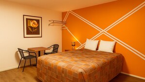 A hotel room with a bed, a desk, two chairs, a framed picture on the wall, and a wall-mounted lamp. - The Pas Motel (The Pas)
