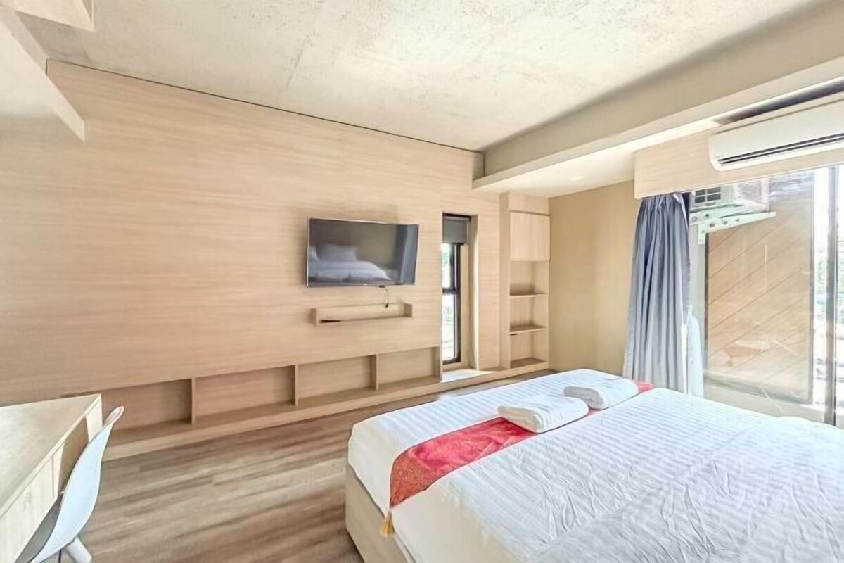 A modern hotel room with a large bed, a flat-screen TV mounted on the wall, and a window with curtains.