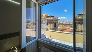 A room with a large window overlooking a cityscape, a radiator, and a small table with a light.