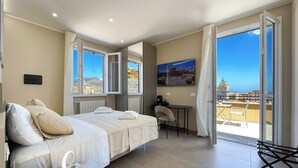 A hotel room with a bed, a desk, a chair, a TV, and a balcony with a view of the city.