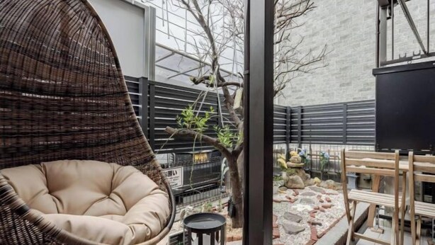 A wicker chair with a cushion, a small table with a black and white mug, and a wooden bench. - Lighthotel-takasago (Tokyo)