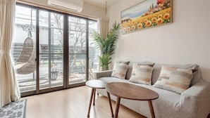 A living room with a sofa, a coffee table, a large window with a view of a garden, and a painting on the wall. - Lighthotel-takasago (Tokyo)
