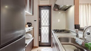 A compact kitchen with a refrigerator, stove, sink, and a door with a window. - Lighthotel-takasago (Tokyo)