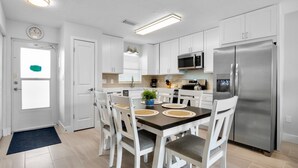Una cocina moderna con armarios blancos, un refrigerador de acero inoxidable y un comedor con mesa y sillas.