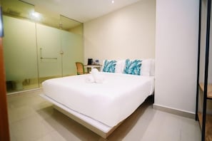Habitación de hotel moderna con una cama grande, cabina de ducha de vidrio y un escritorio pequeño con silla.