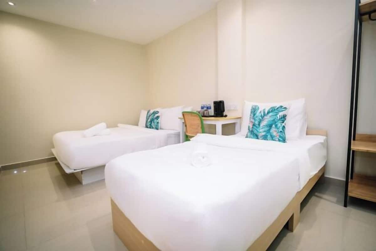 A hotel room with two single beds, a small table with a chair, and a shelf unit.