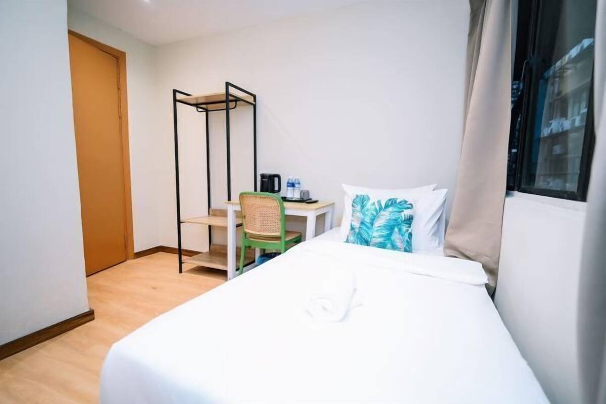 A hotel room with a bed, a desk with a chair, a window, and a door.